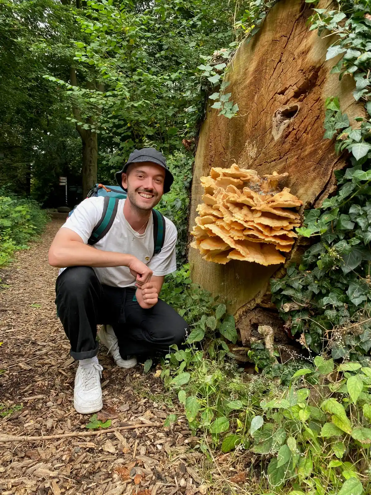 Aiden Buis gehurkt naast een grote zwavelzwam op een boomstronk in het bos.